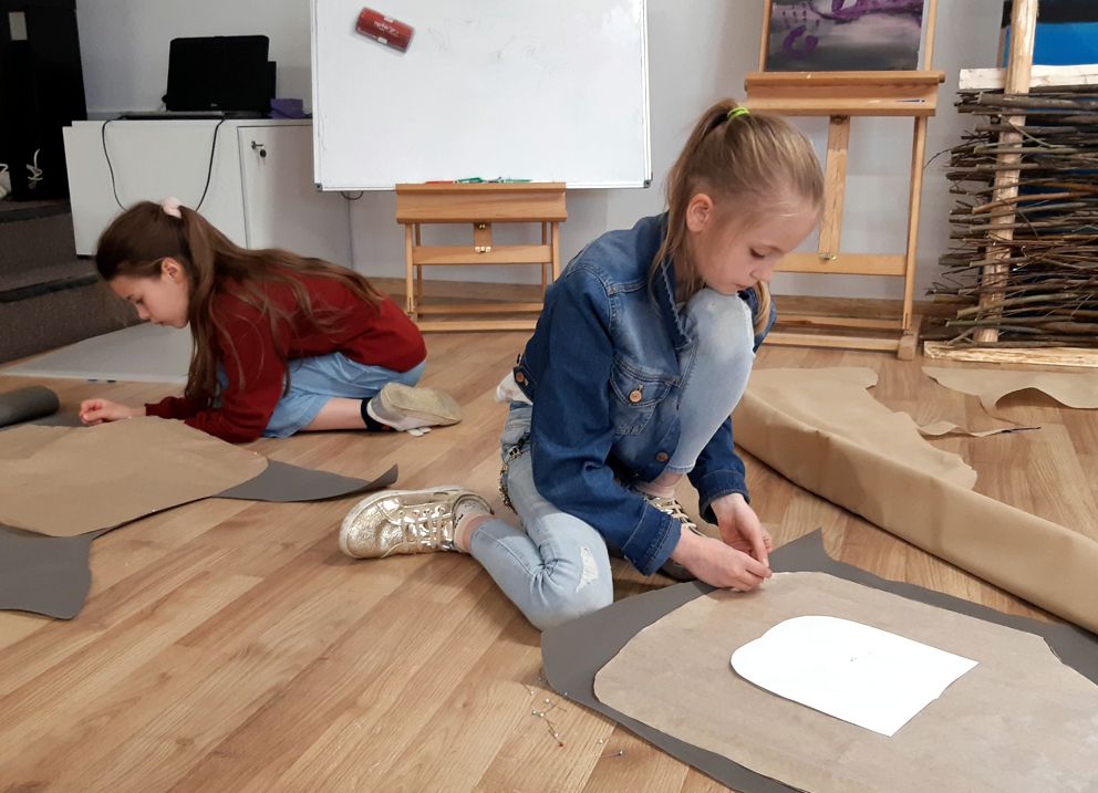 dwie dziewczynki na podłodze projektuja z papieru formę fartuszka